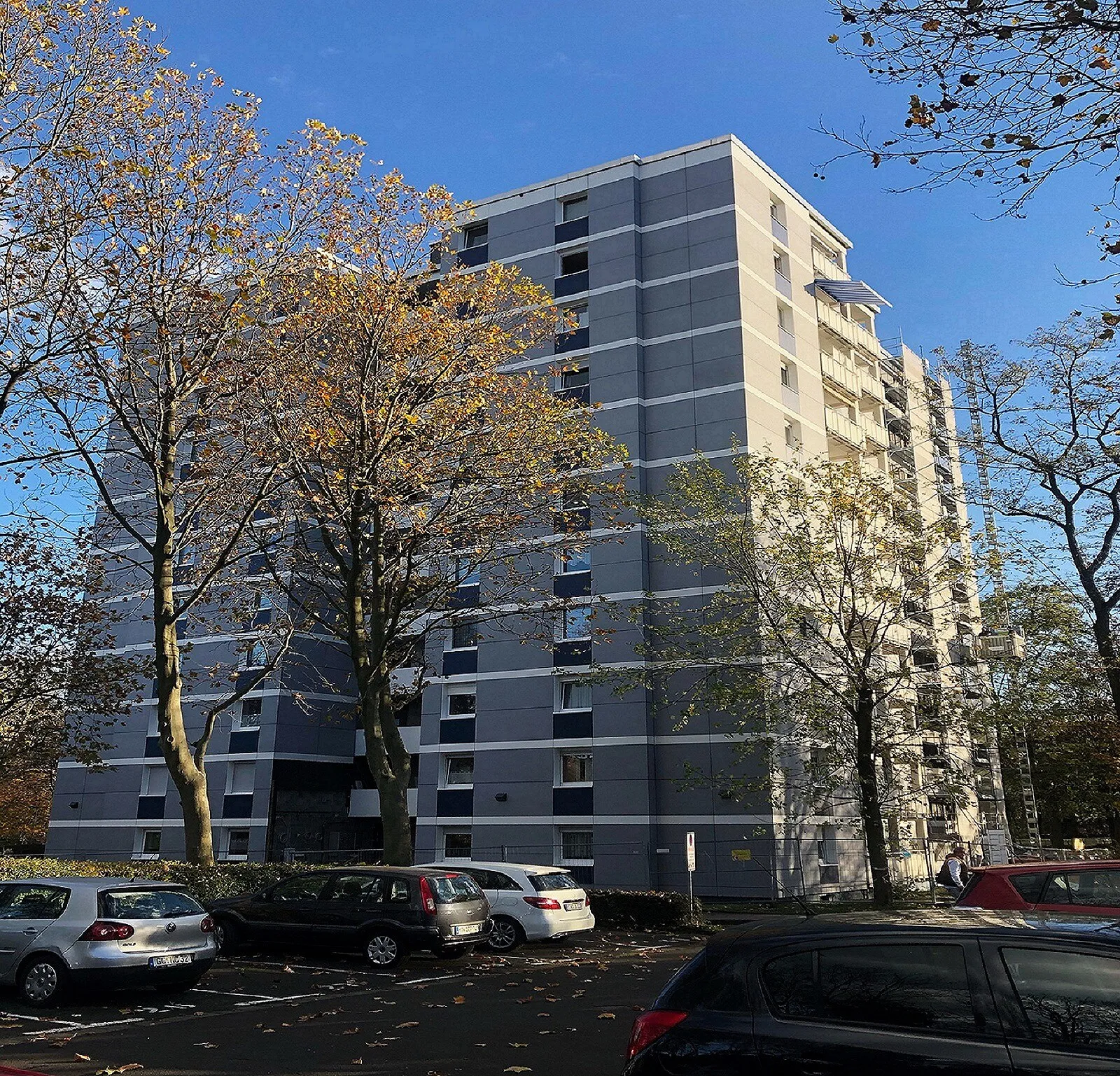 Wohnhochhaus in Eschborn mit blaugrauer Plattenfassade, im Vordergrund Bäume mit Herbstlaub